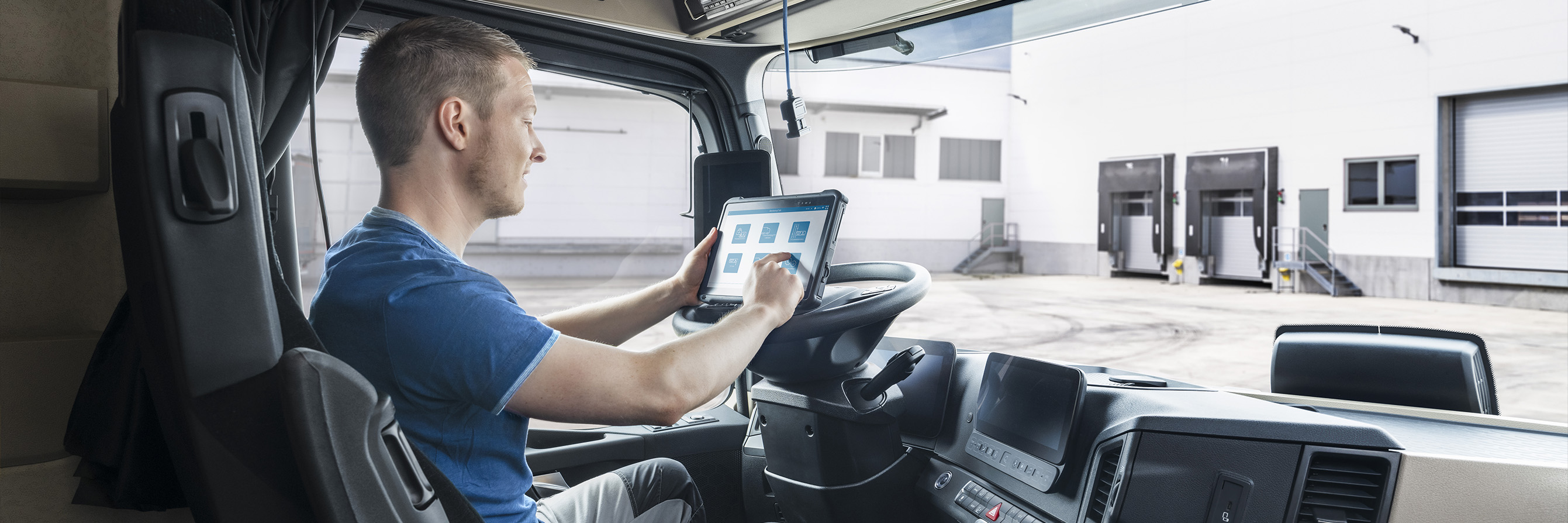 Picture taken from the passenger seat of a truck. In the picture you can see a fleet driver parked in his employer's yard, operating a tablet running a VDO software.